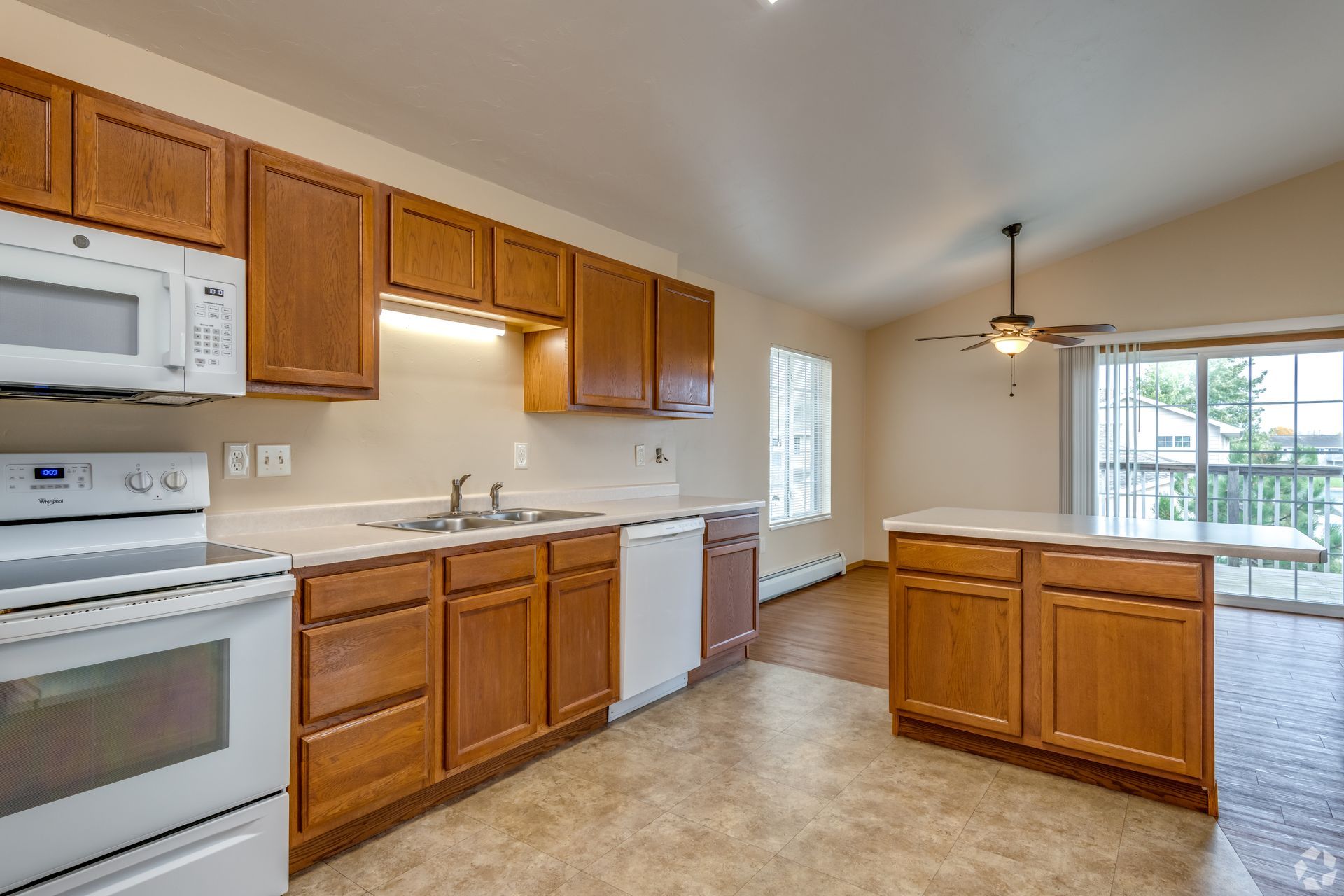 Bright kitchen with wood cabinets, white appliances, and a central island near a windowed dining area