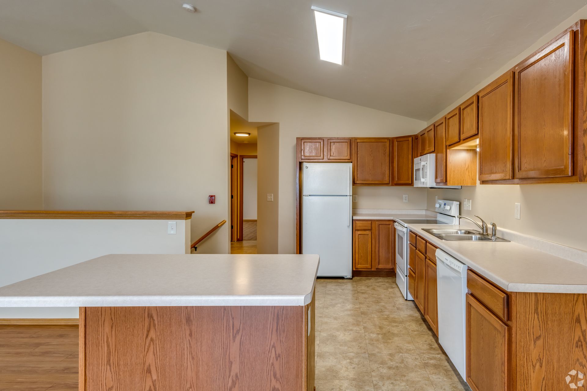 Empty kitchen with wooden cabinets, white appliances, and a peninsula counter under bright overhead lights