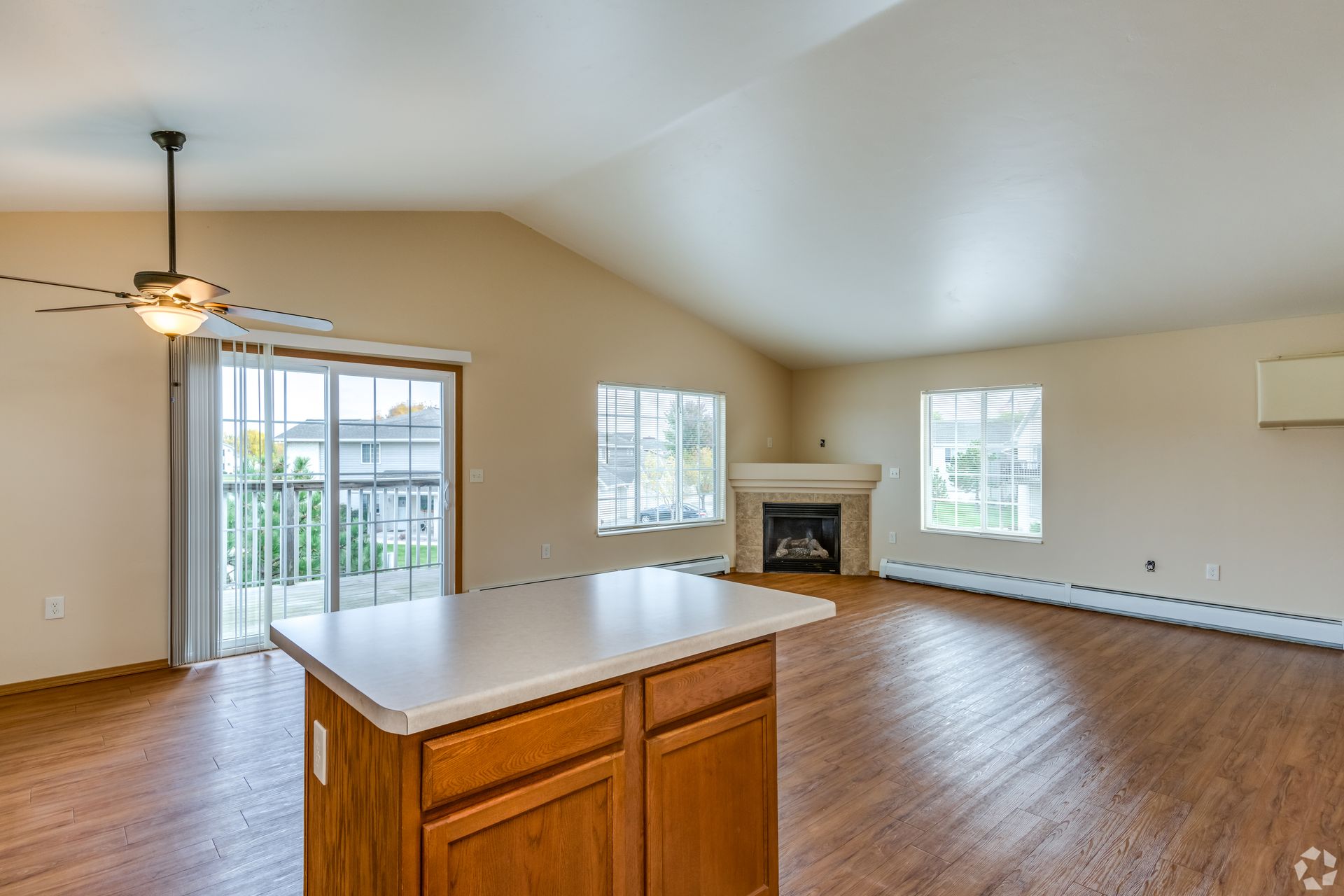 Empty living room with hardwood floors, vaulted ceiling, fireplace, and sliding glass doors to a balcony.