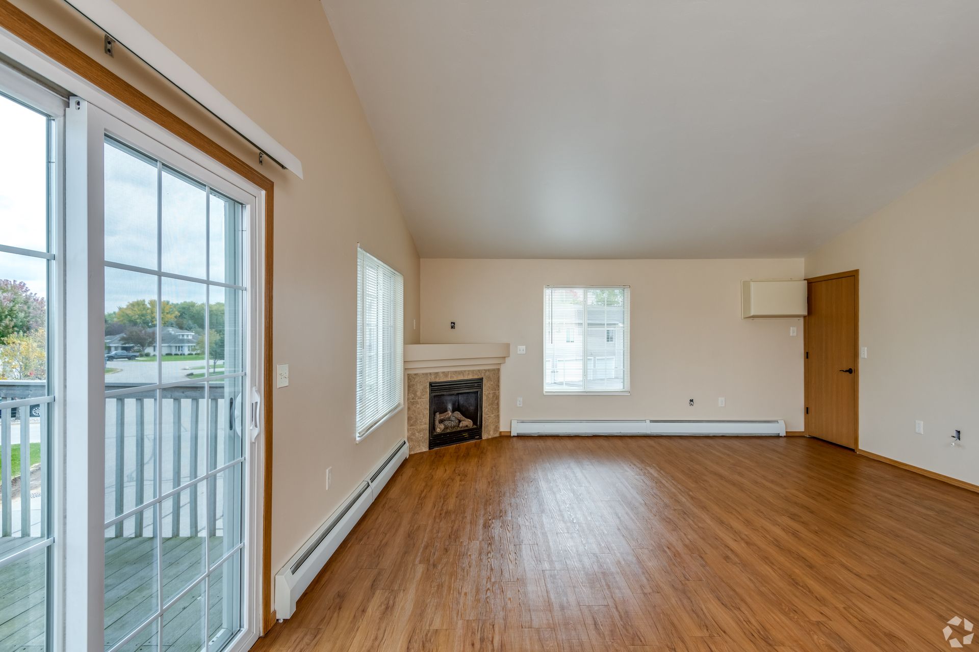 Spacious empty living room with hardwood floors, fireplace, and sliding glass doors to a balcony.