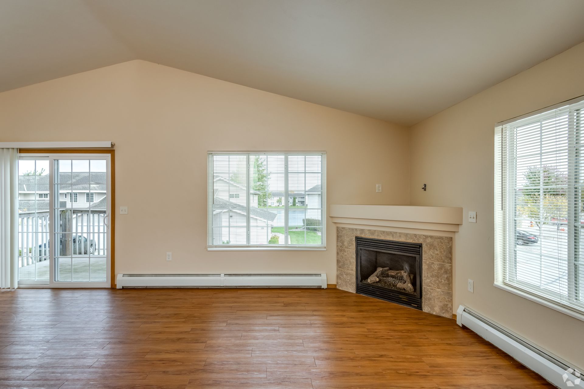 Empty living room with hardwood floors, beige walls, fireplace, and sliding glass doors