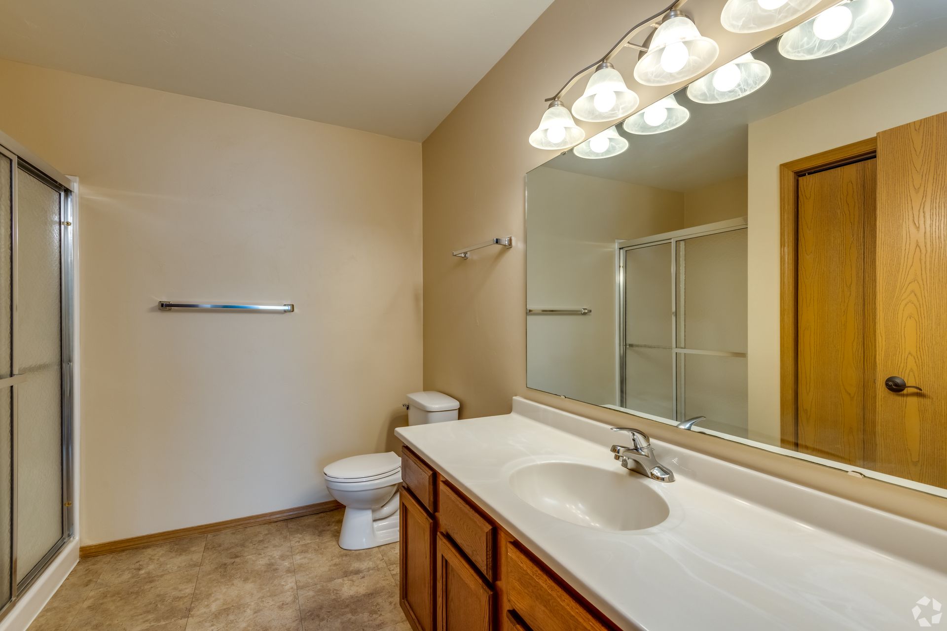 Bathroom with vanity, large mirror, toilet, shower, and beige walls.