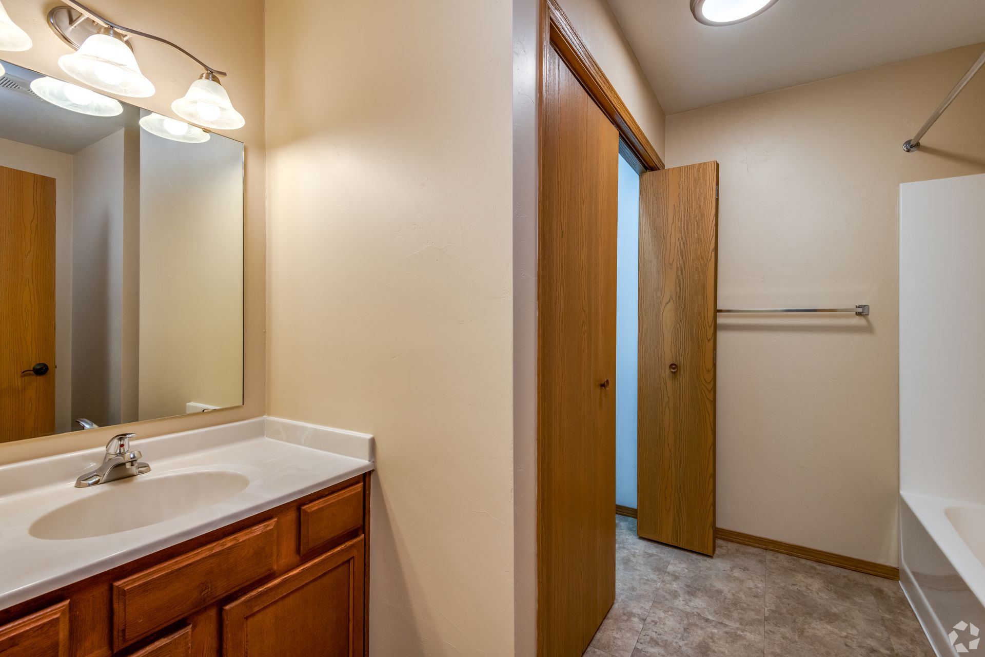 Bathroom vanity and hallway with open wooden door, beige walls, and a towel bar.