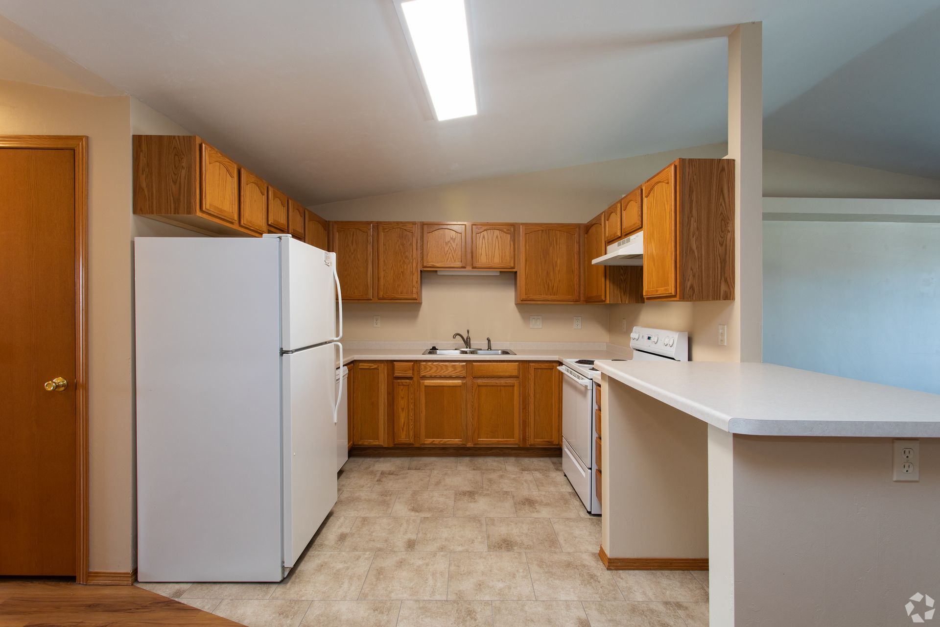 Empty kitchen with wood cabinets, white appliances, and a light tile floor.