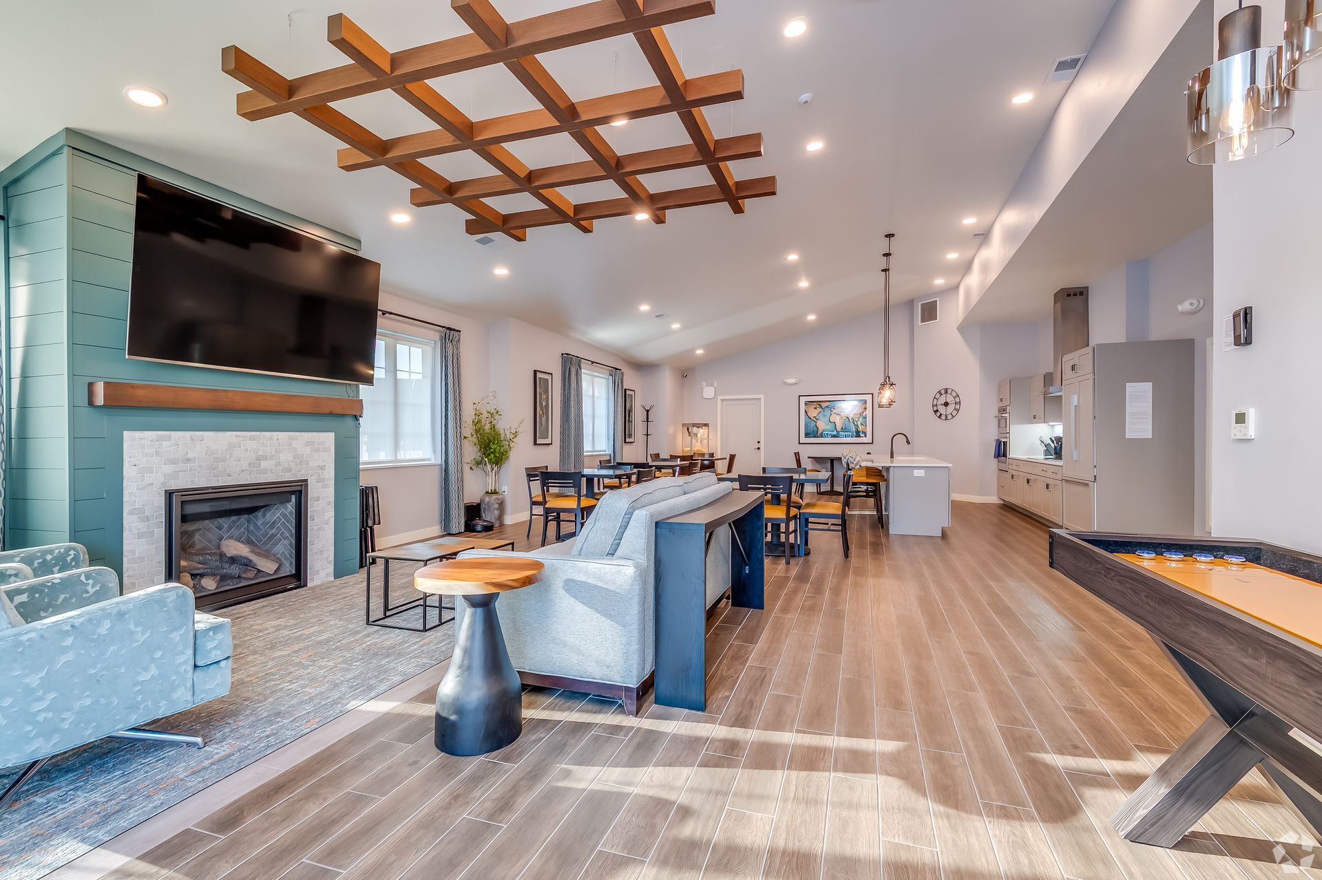 Modern living room with fireplace, wall TV, blue sofas, wood ceiling accents, and dining area