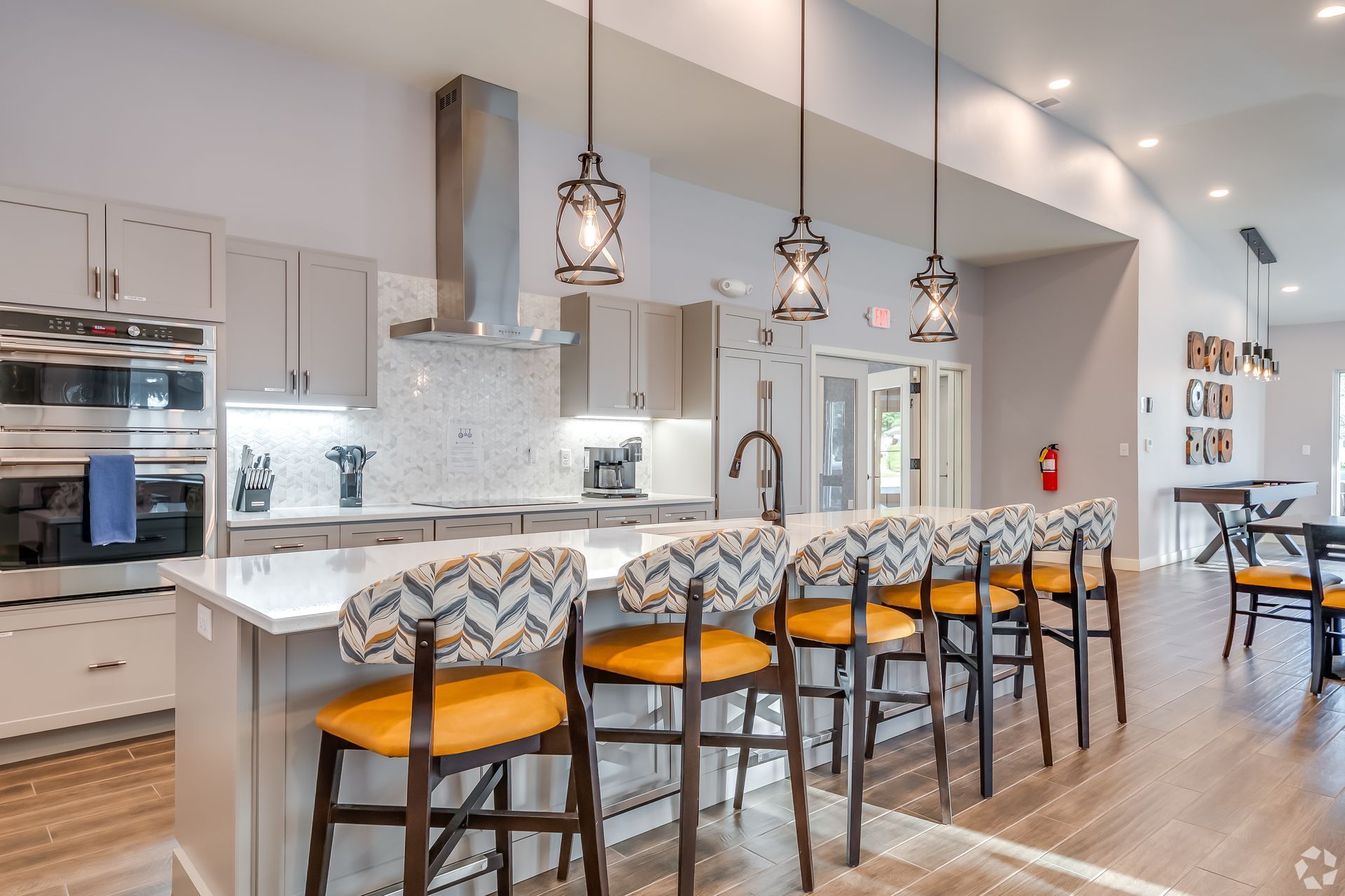 Modern kitchen with island, pendant lights, and orange-accented barstools leading into a bright open dining area