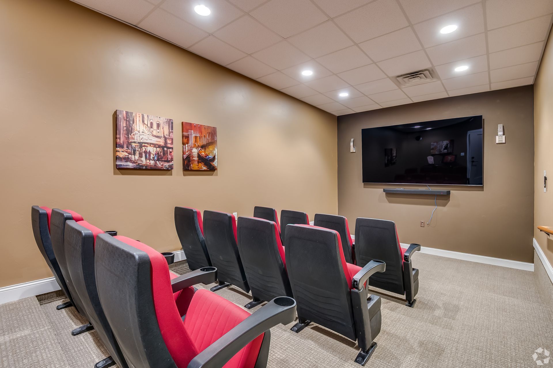 Modern media room with rows of black-and-red seats facing a wall-mounted TV.