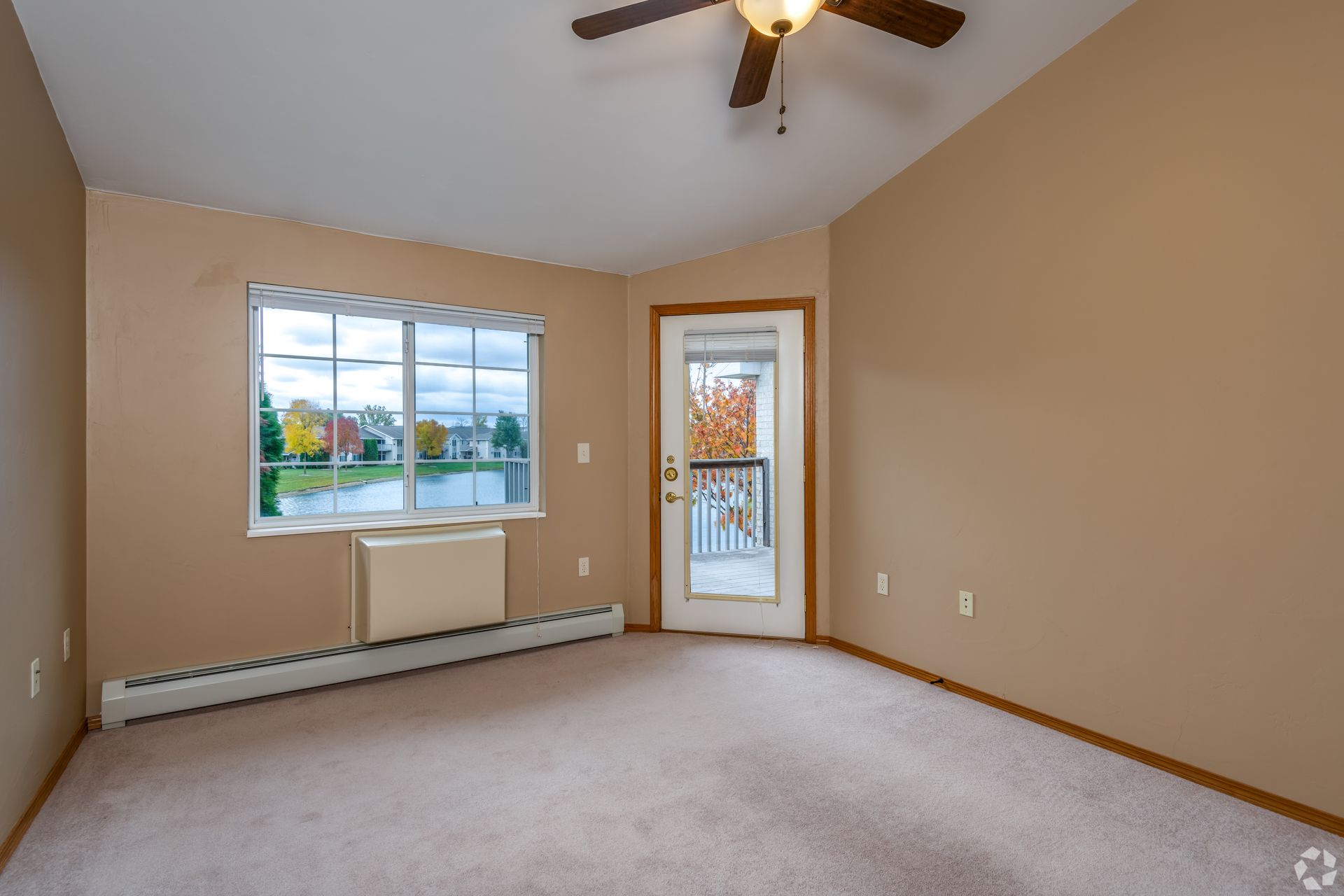 Empty beige bedroom with a window, glass door, ceiling fan, and carpeted floor