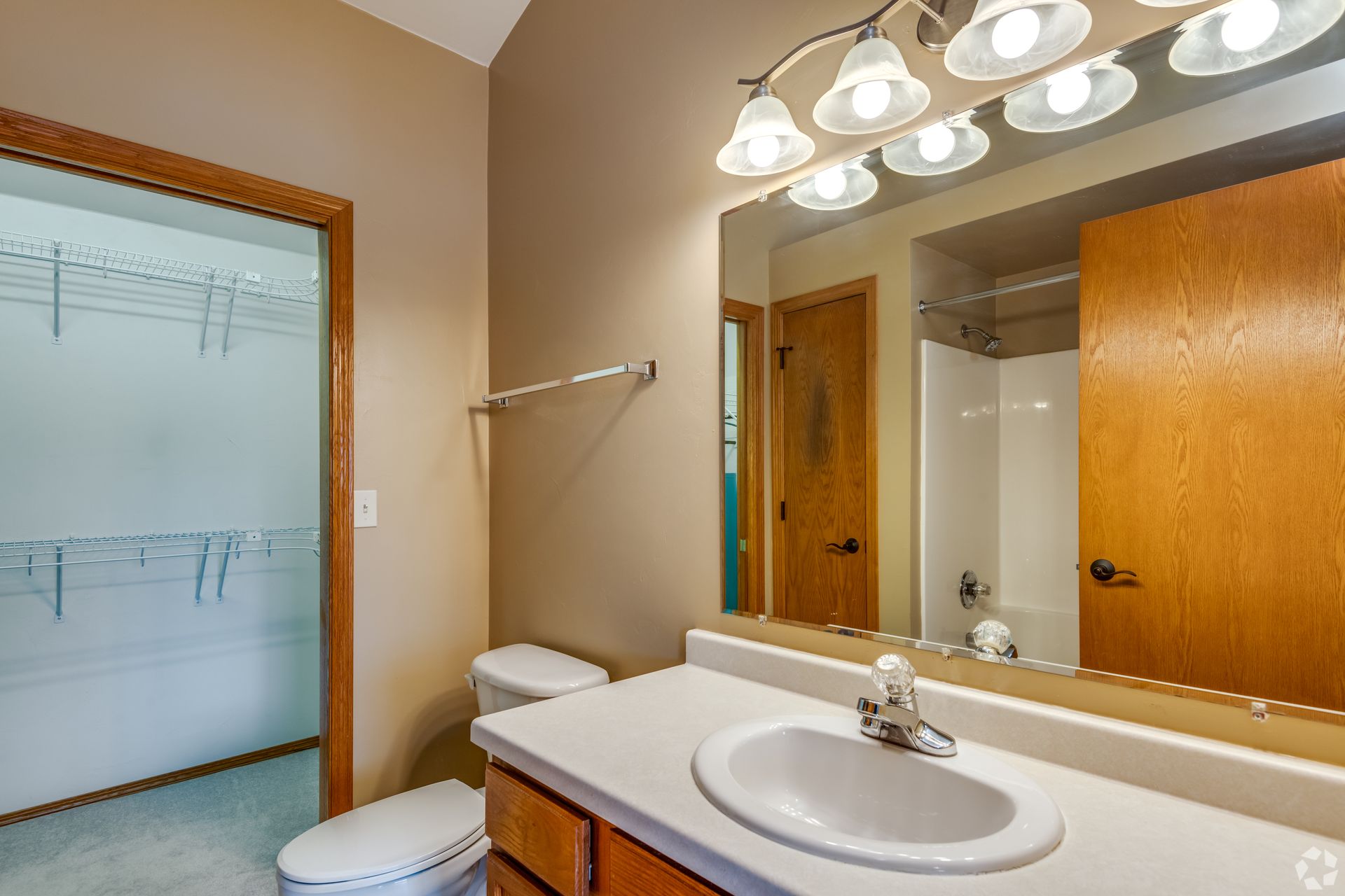 Bathroom with white sink, wooden vanity, large mirror, shower curtain, and hanging light fixture.