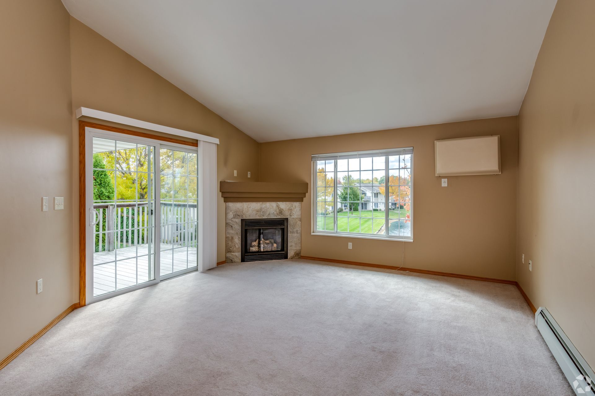 Empty living room with beige walls, fireplace, carpet, and sliding glass door to a balcony