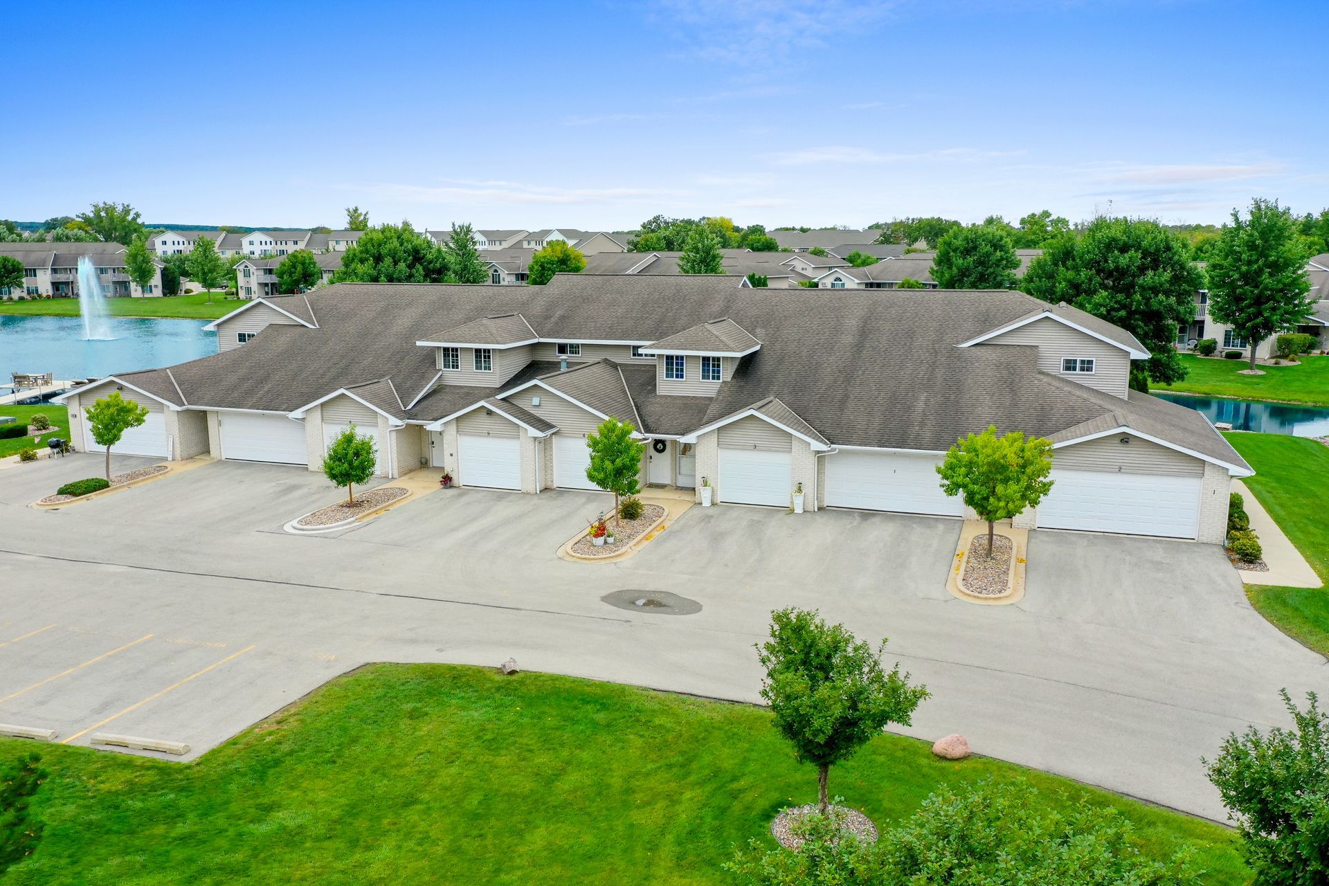 Aerial view of a large beige apartment complex with garages, parking lot, and green lawn