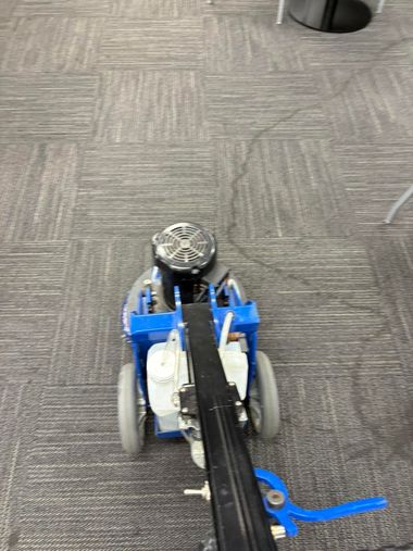 Blue-and-white small robot on carpet, with a black arm extending forward and a blue cable beside it