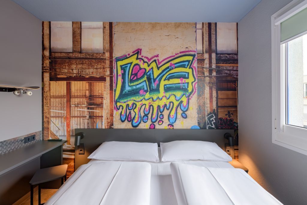 Modernes Schlafzimmer mit zwei Einzelbetten und einem farbenfrohen Wandbild im Graffiti-Stil über dem Kopfteil