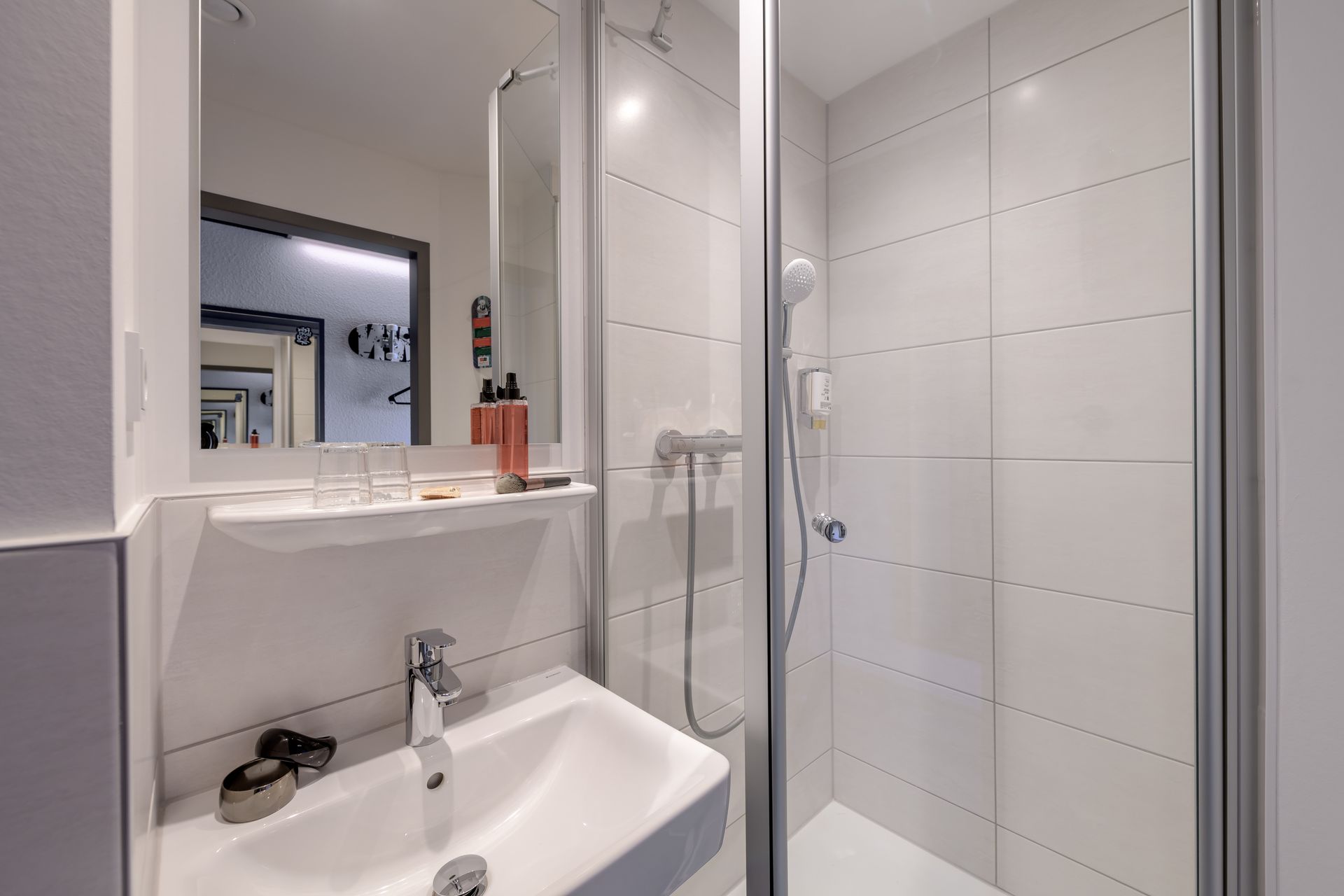 Kleines, modernes Badezimmer mit weißem Waschbecken, Spiegel und Duschkabine aus Glas