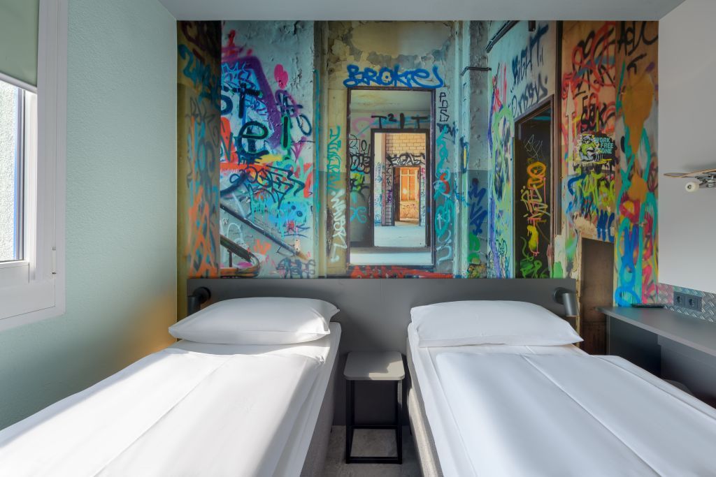 Zentrale Unterkunft mit zwei Einzelbetten und einem farbenfrohen Wandgemälde im Graffiti-Stil an der Rückwand.