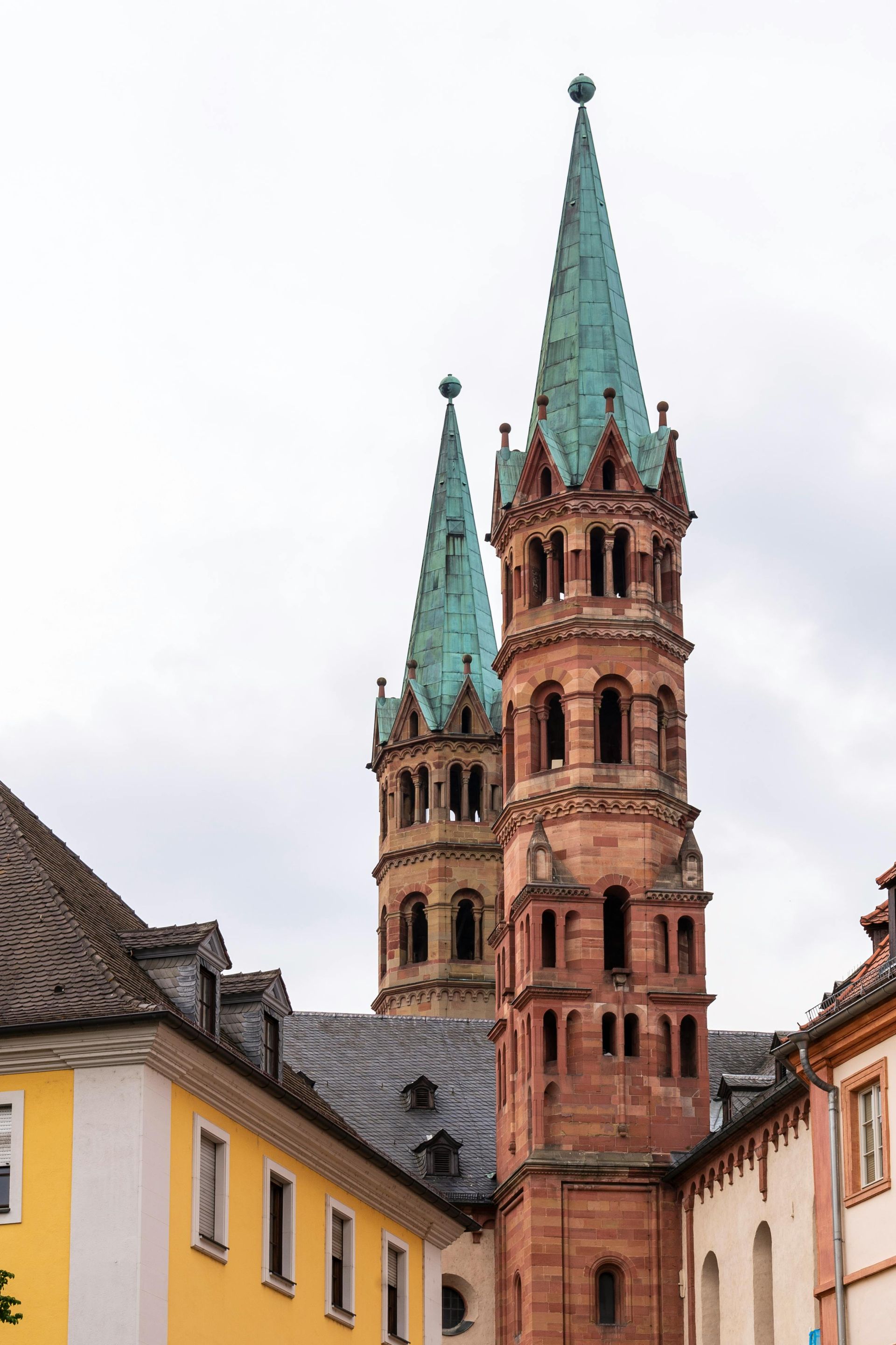 Historische Backsteinkirchentürme mit grünen Turmspitzen über farbenfrohen alten Gebäuden unter einem bewölkten Himmel