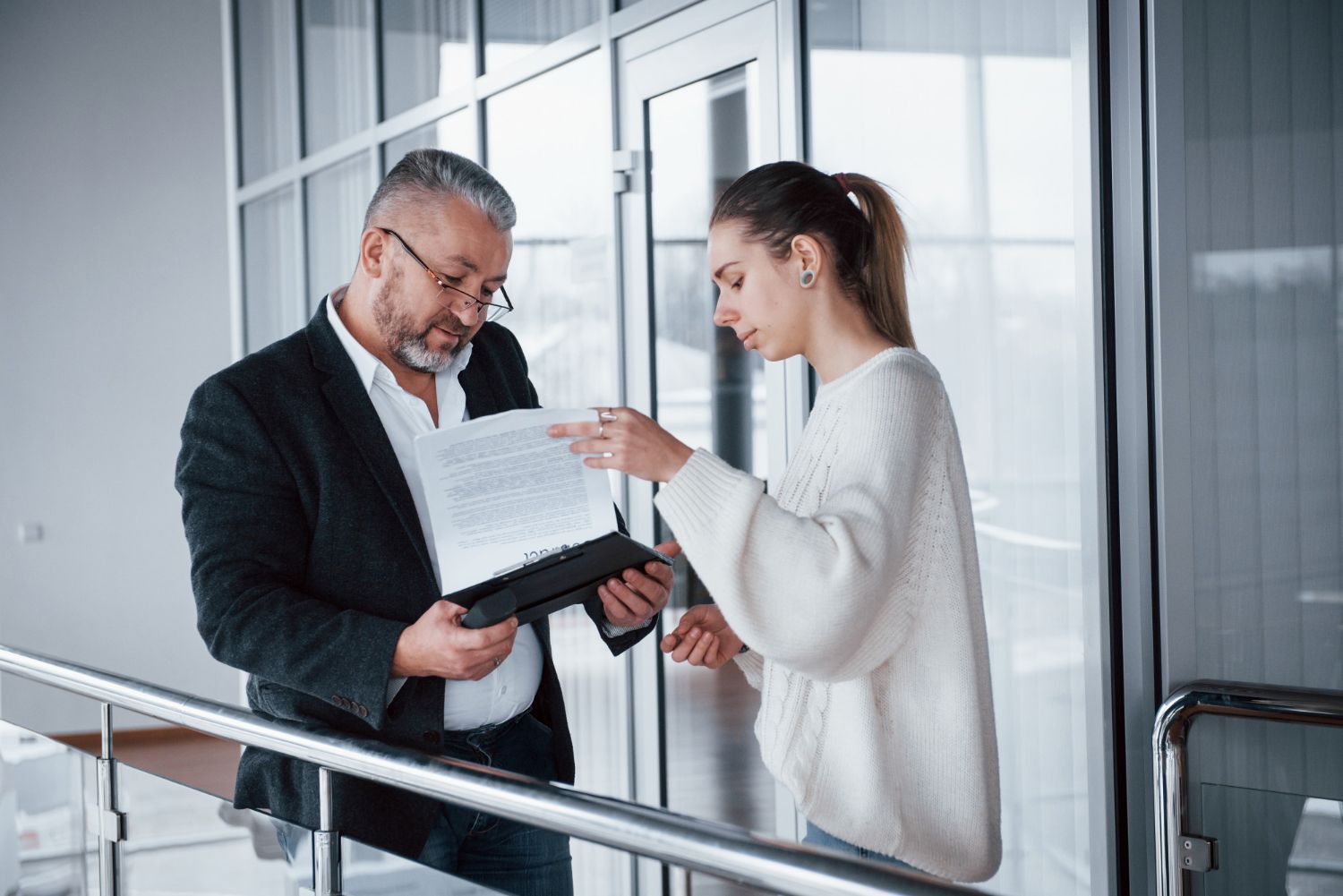 Two coworkers reviewing documents together in a bright office hallway