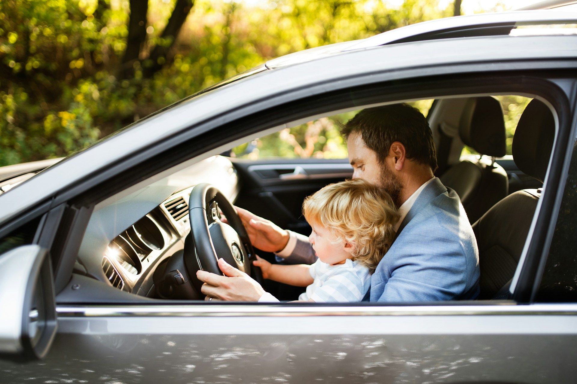 Adult teaching child to drive in a car, both holding the steering wheel