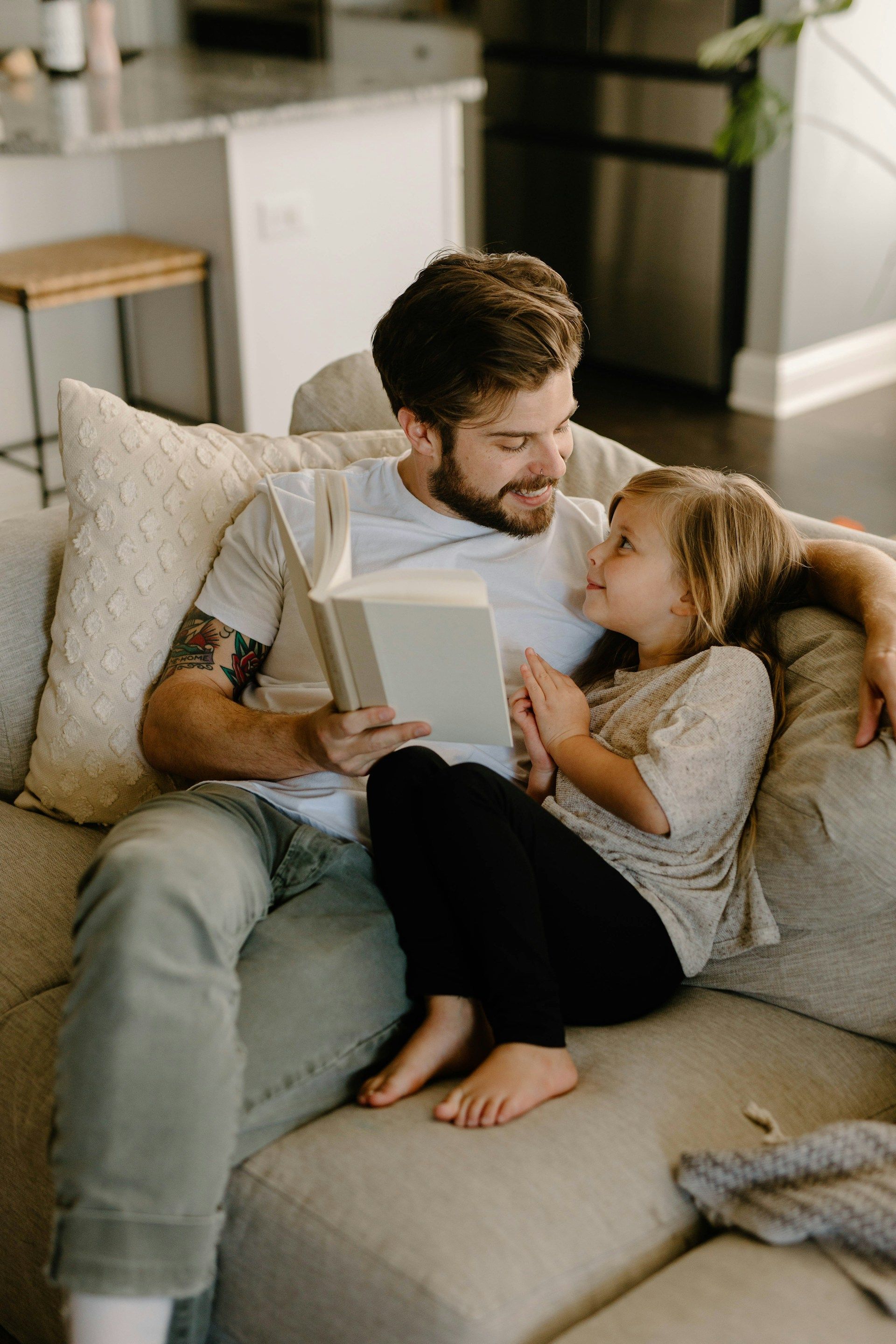 Couple cuddling on a couch, reading a book together in a cozy living room.