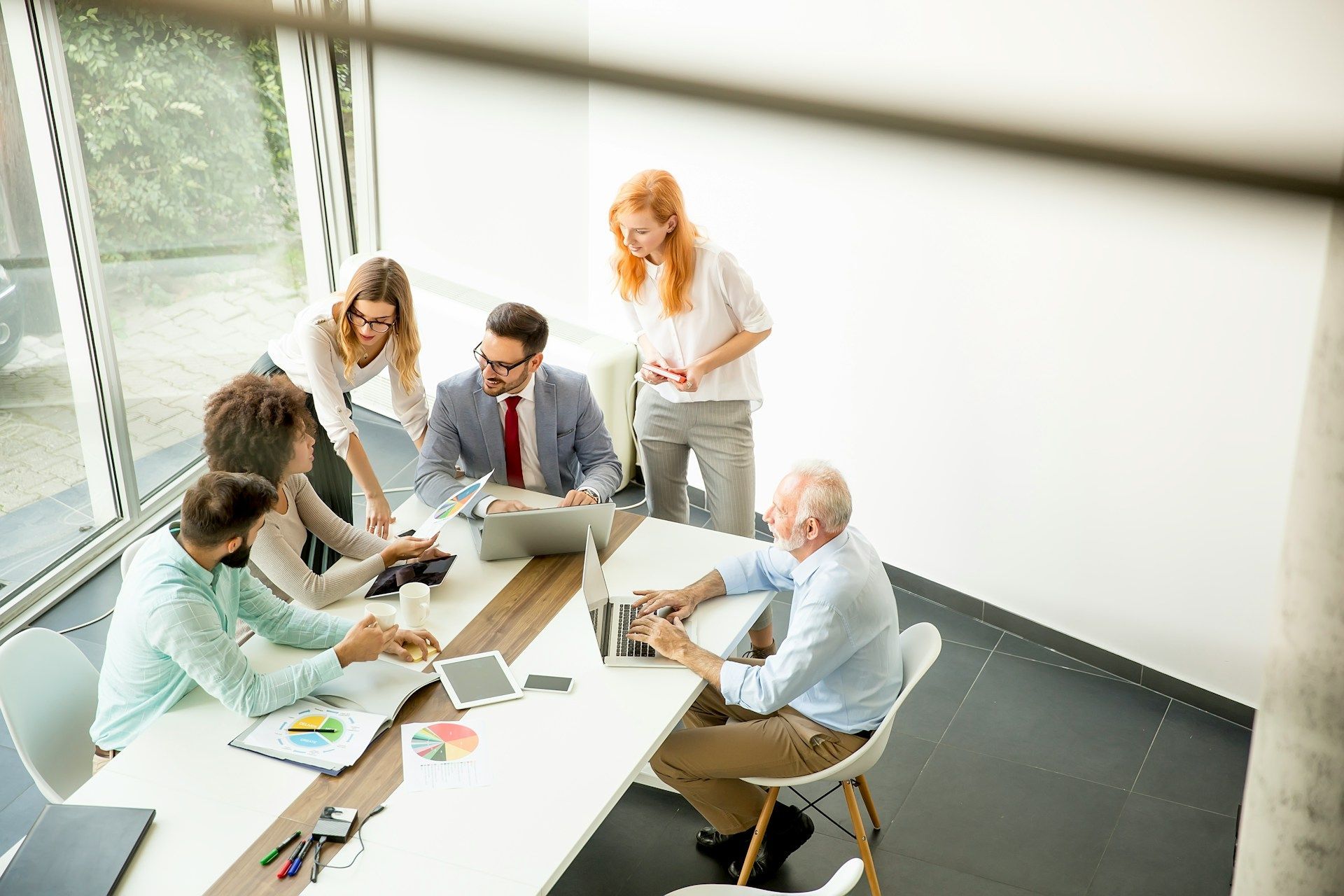 Team meeting around a laptop in a bright office, with papers and charts spread on the table.