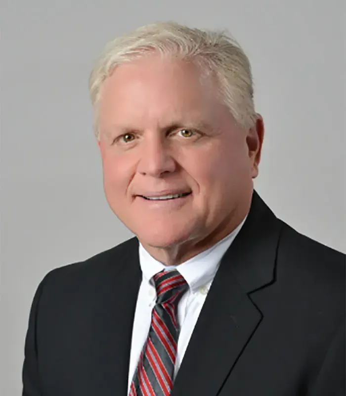 Portrait of a man in a black suit and red striped tie against a gray background