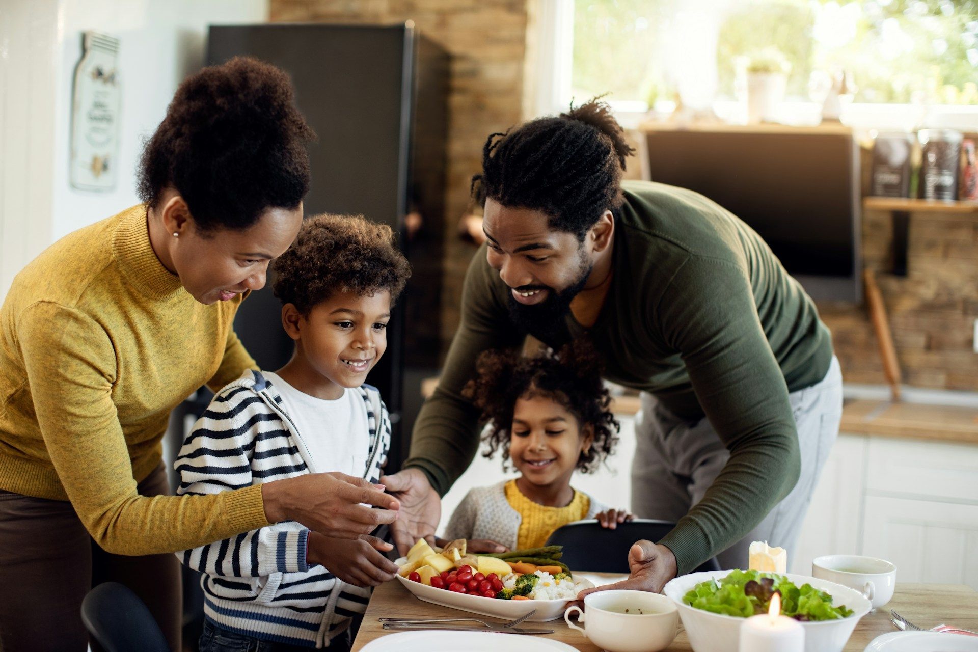 Family gathered around a dining table, smiling while serving a meal in a warm kitchen.