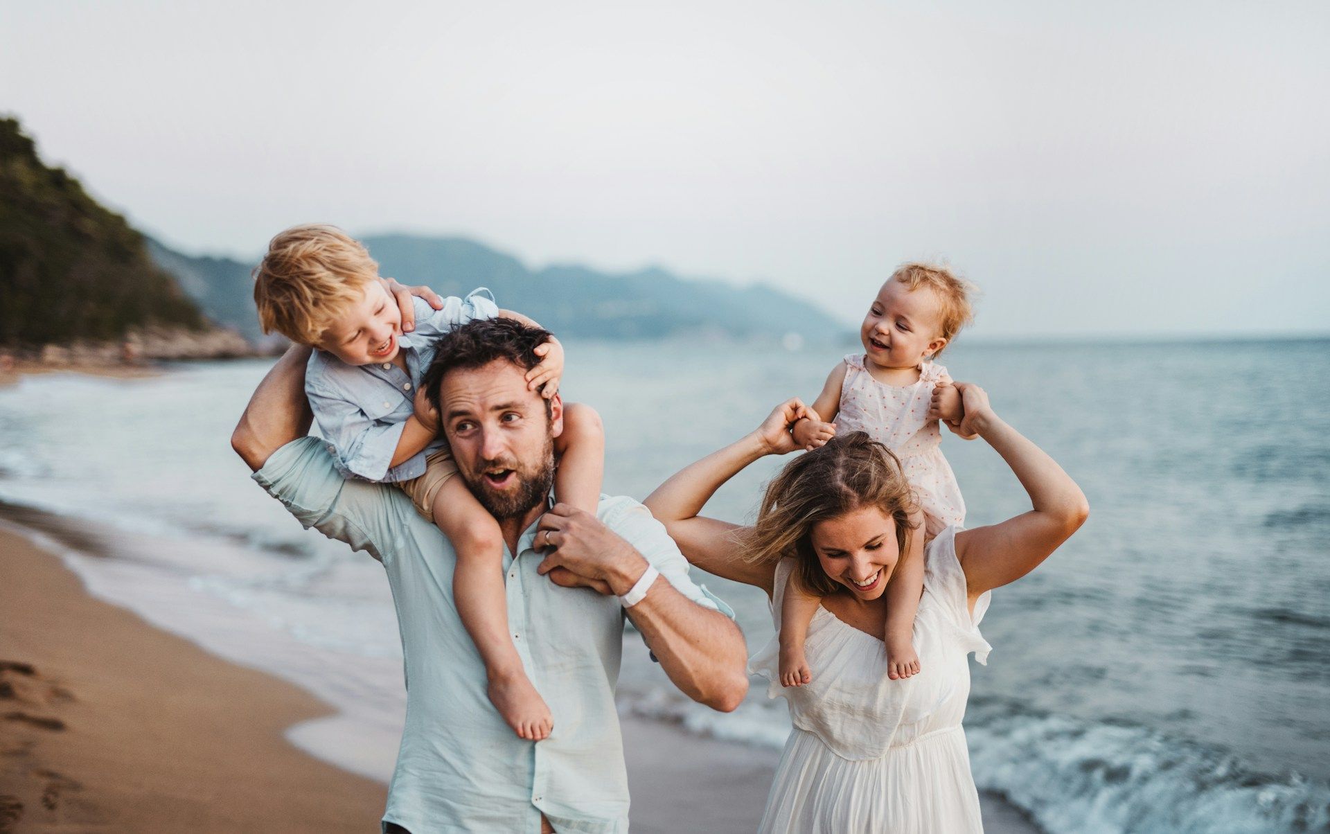 Family walking along a beach, children on parents’ shoulders by the shoreline