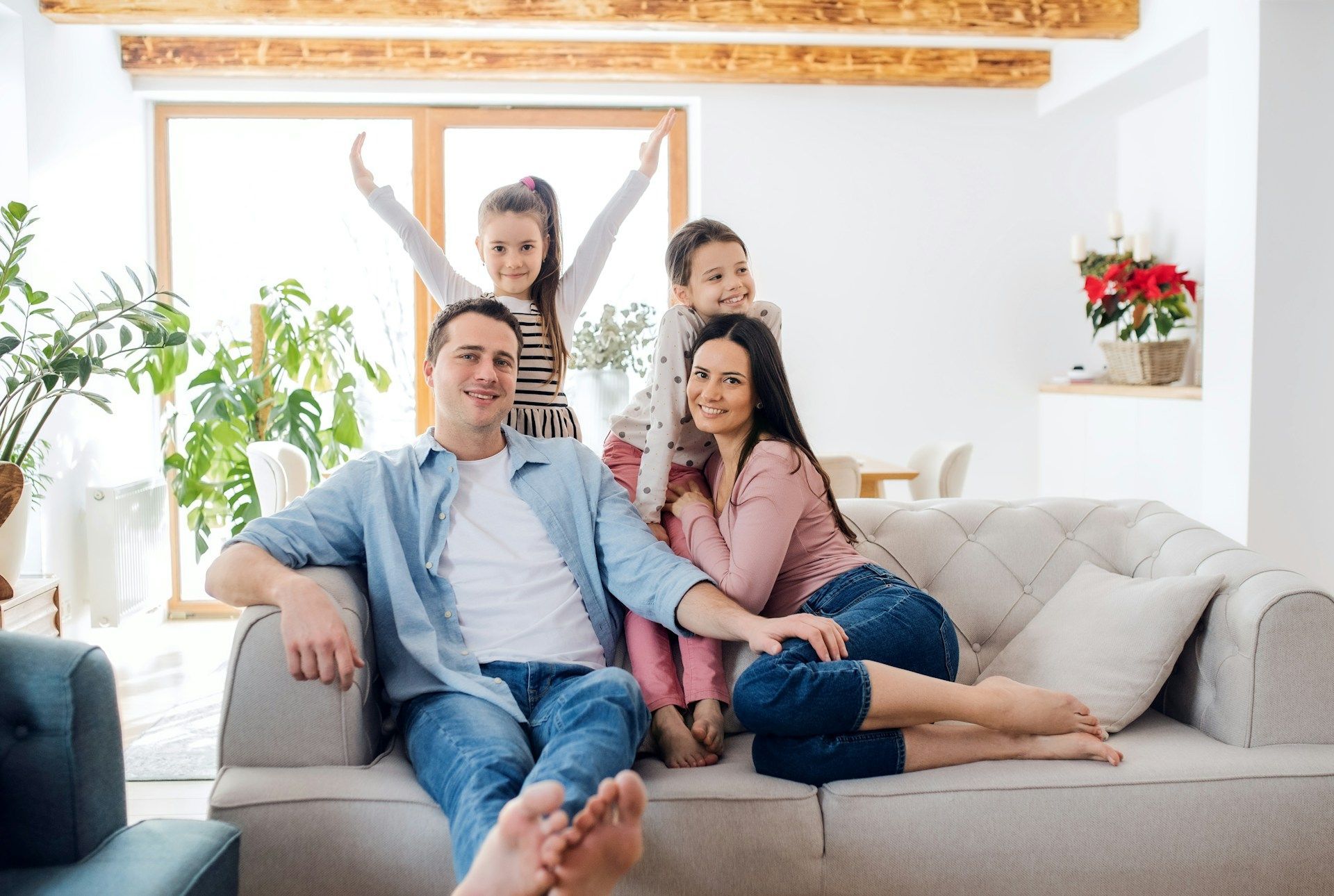 Family relaxing together on a couch in a bright living room, with a child standing behind them.