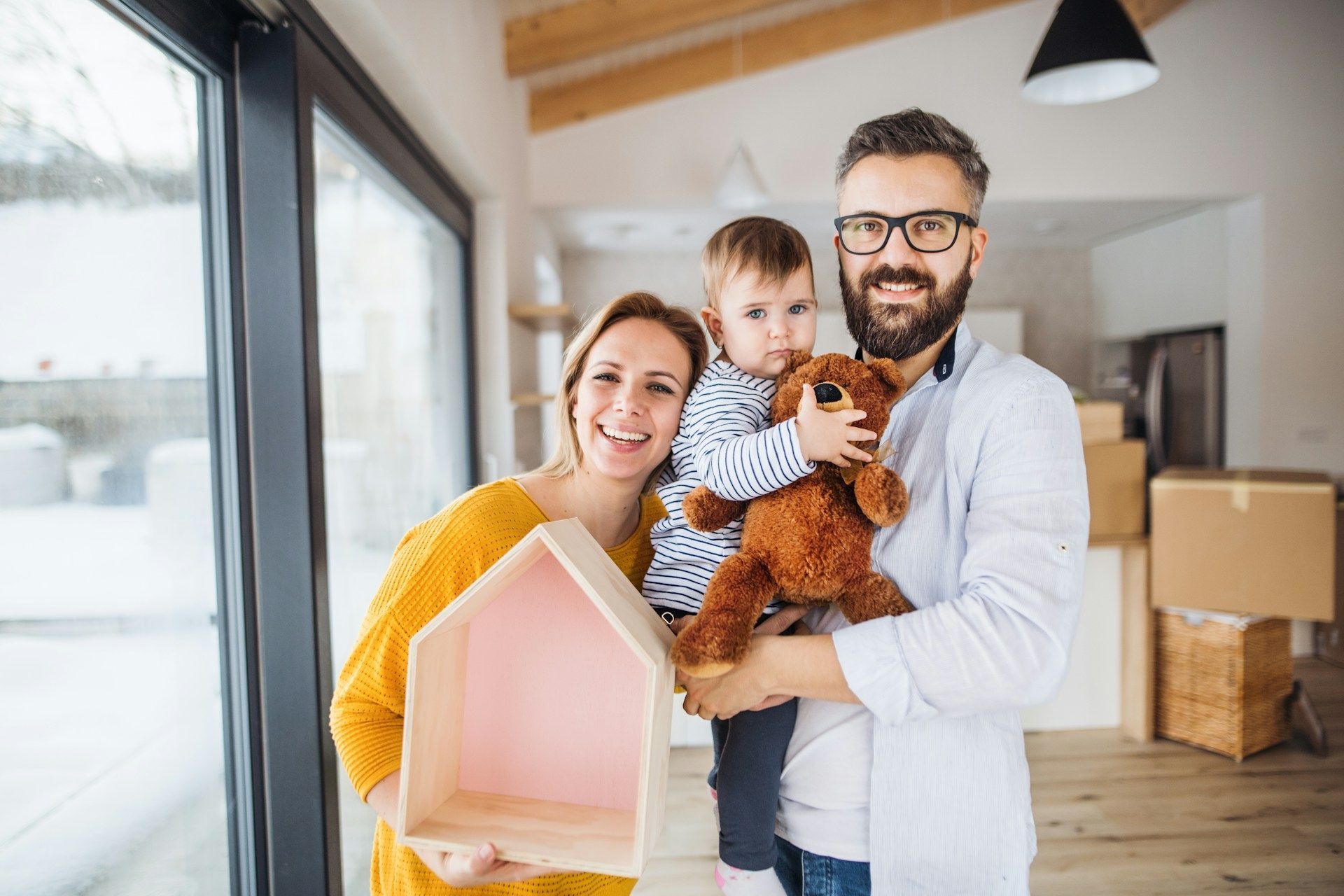 Family holding house model and teddy bear in a bright moving-home room