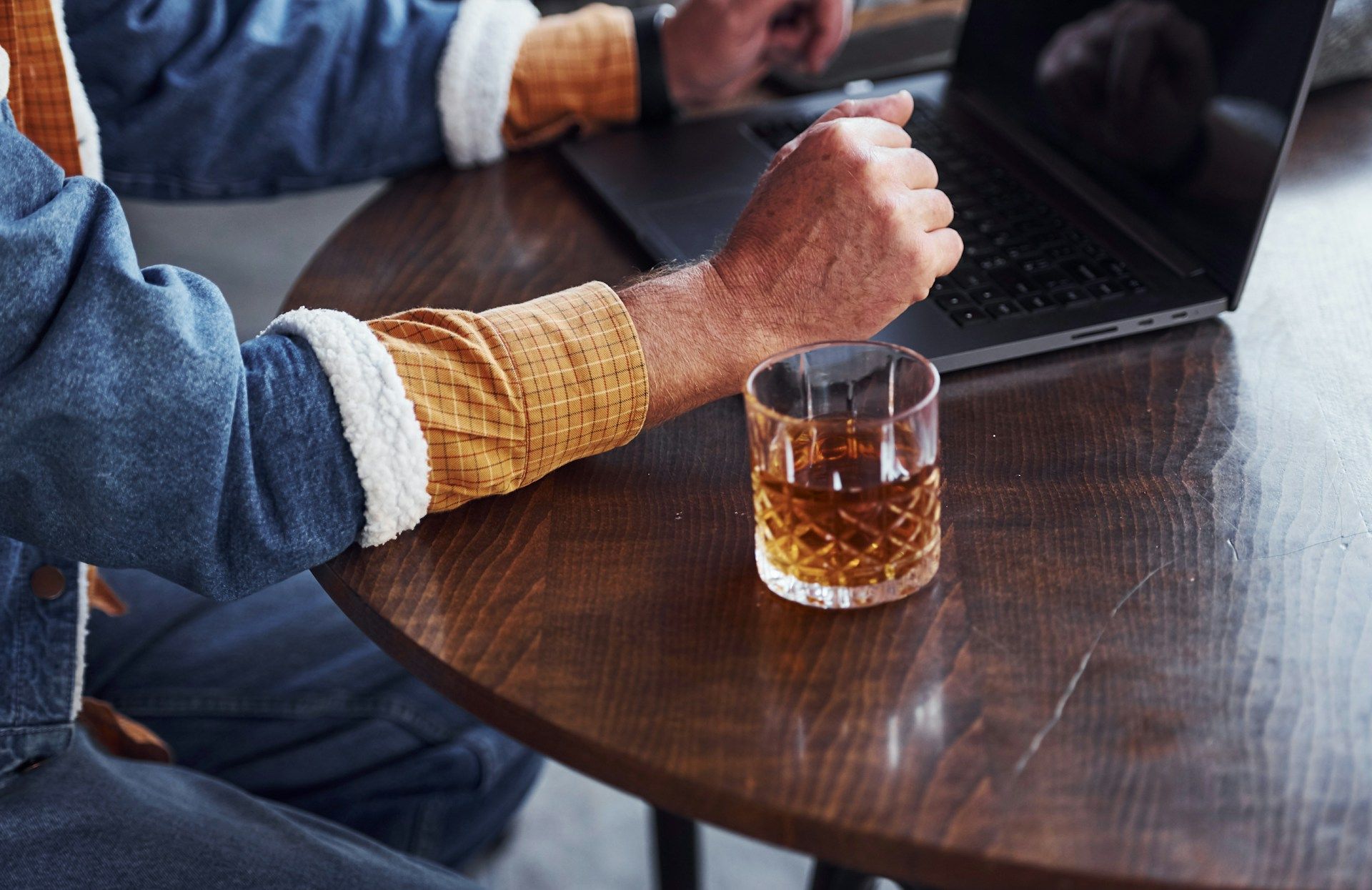 Person at a table using a laptop and stirring a drink in a glass tumbler