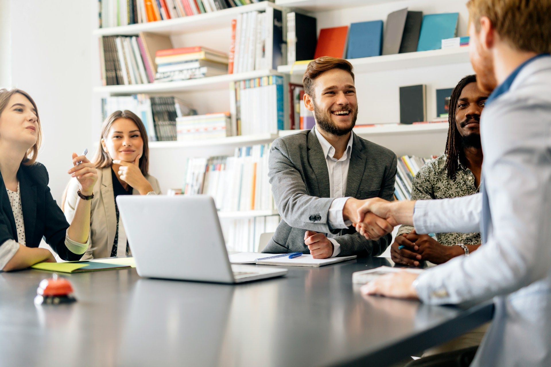 Business meeting around a conference table with a laptop, notebooks, and people shaking hands in an office