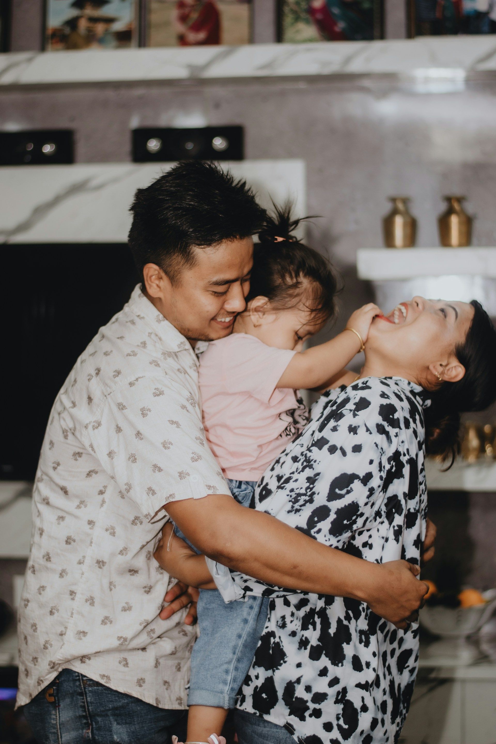 A family hugging in a kitchen, with a child between two smiling adults.