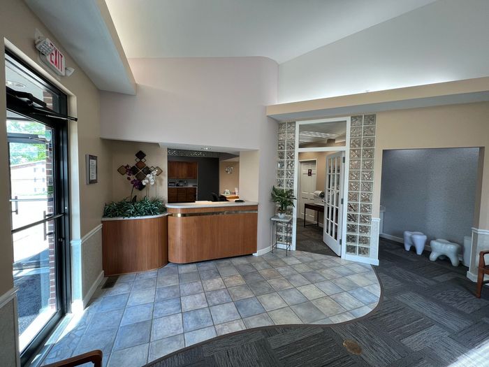 A professional dental office reception area with a wood-paneled desk, tiled flooring, and a glass-paneled entry door.