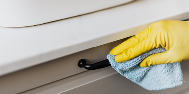 Yellow gloved hand wiping a white cabinet handle with a blue cloth