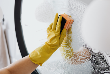 Gloved hand cleaning a fogged bathroom mirror with a sponge