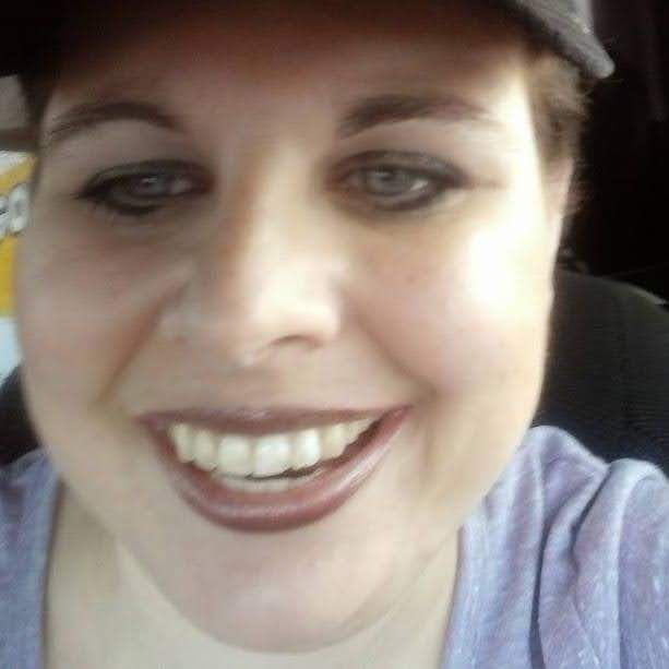 Close-up selfie of a smiling person wearing a cap and purple shirt.