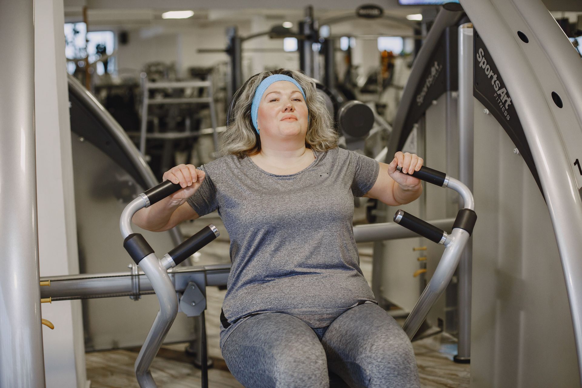 Person doing a V-up on a blue mat in a gym, with weights and exercise equipment in the background