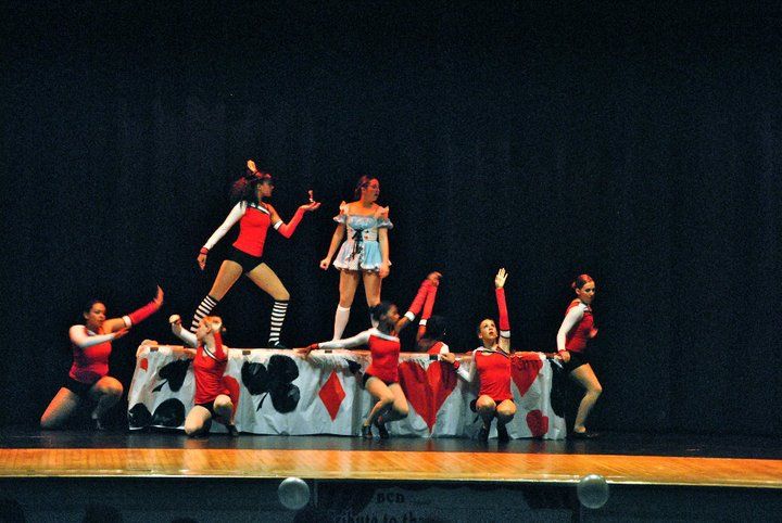 Five dancers in stage performance; acrobatic pose with split, leg splits, and red and black costumes.