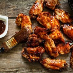 Chicken wings are sitting on a wooden table next to a bowl of barbecue sauce.