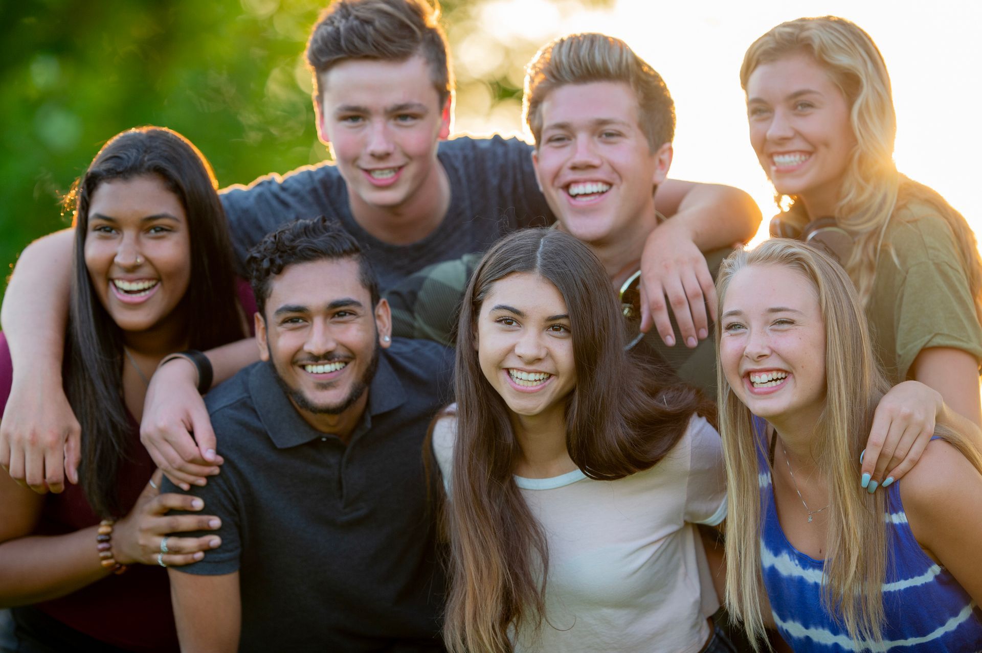 Group of smiling people posing outdoors. Warm sunlight.