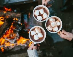 Three people are holding cups of hot chocolate with marshmallows in front of a fire. Three people are holding cups of hot chocolate with marshmallows in front of a fire.