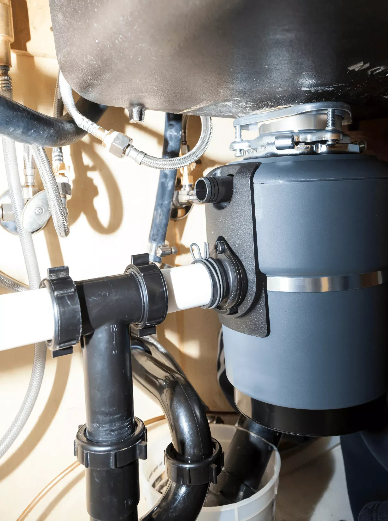 Garbage disposal unit installed under a kitchen sink with drain pipes connected in a Bakersfield home