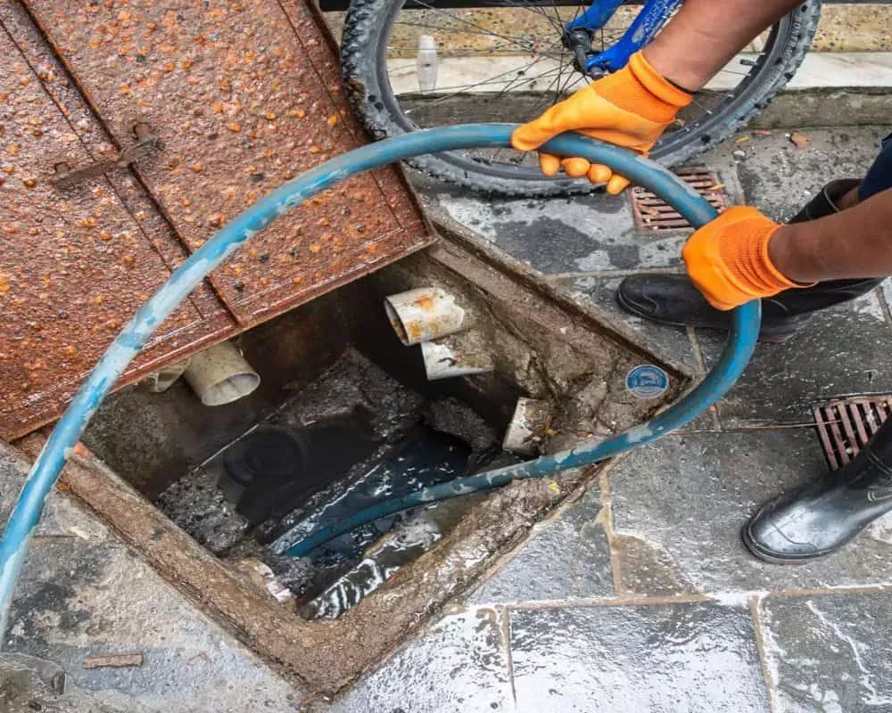 Plumber feeding a hydro jetting hose into a residential drain cleanout to clear a blockage in Bakersfield CA