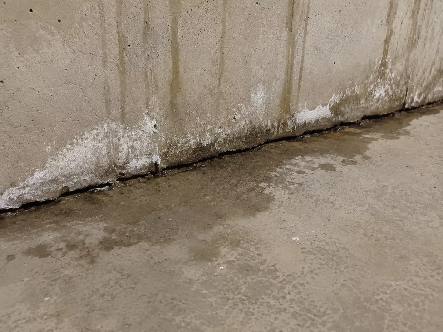 Water seeping through a cracked concrete wall and floor joint showing signs of an active slab leak in Bakersfield CA
