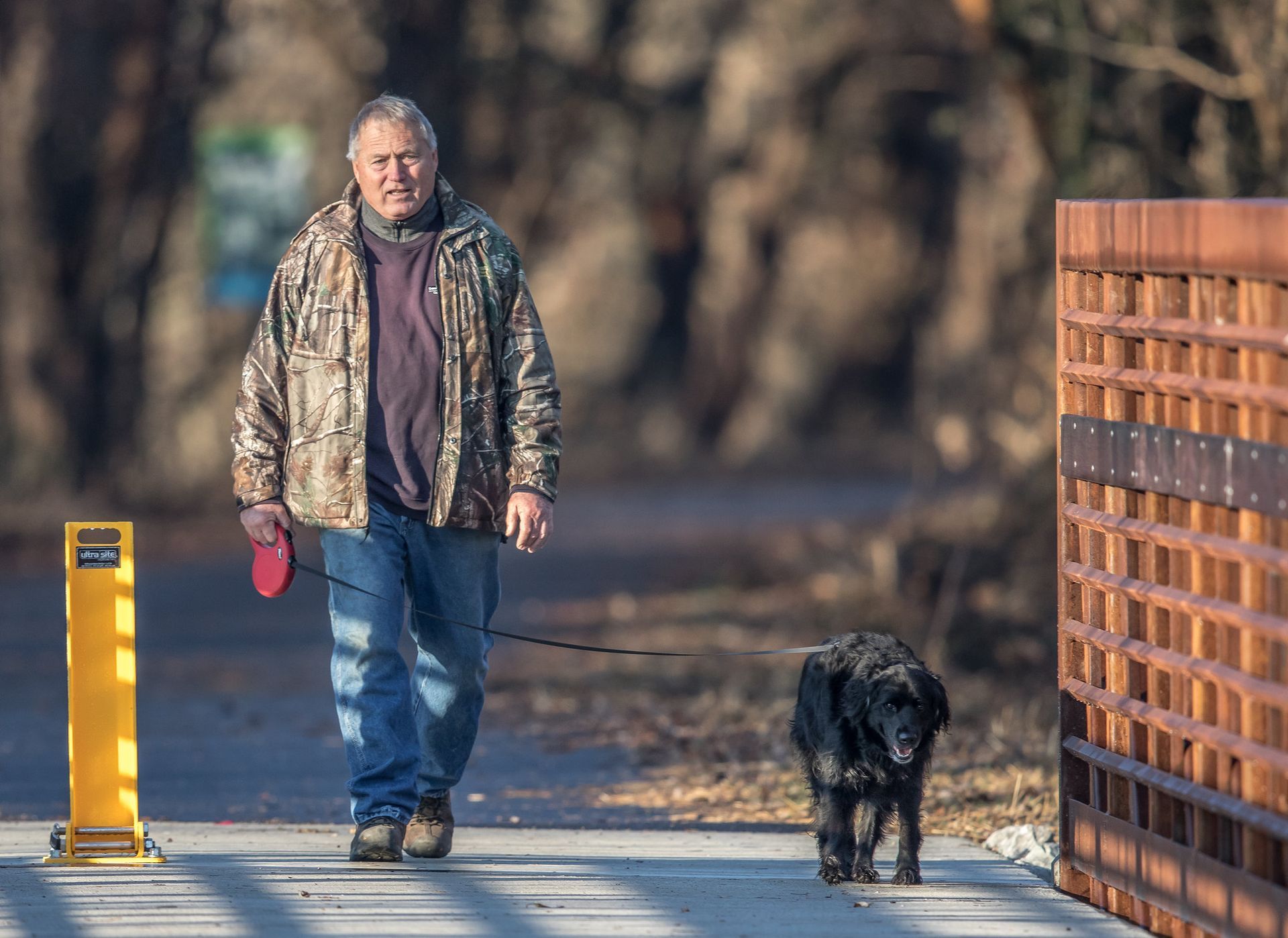 Man in camo jacket walks dog on the Ohio River Greenway bridge crossing over Silver Creek.