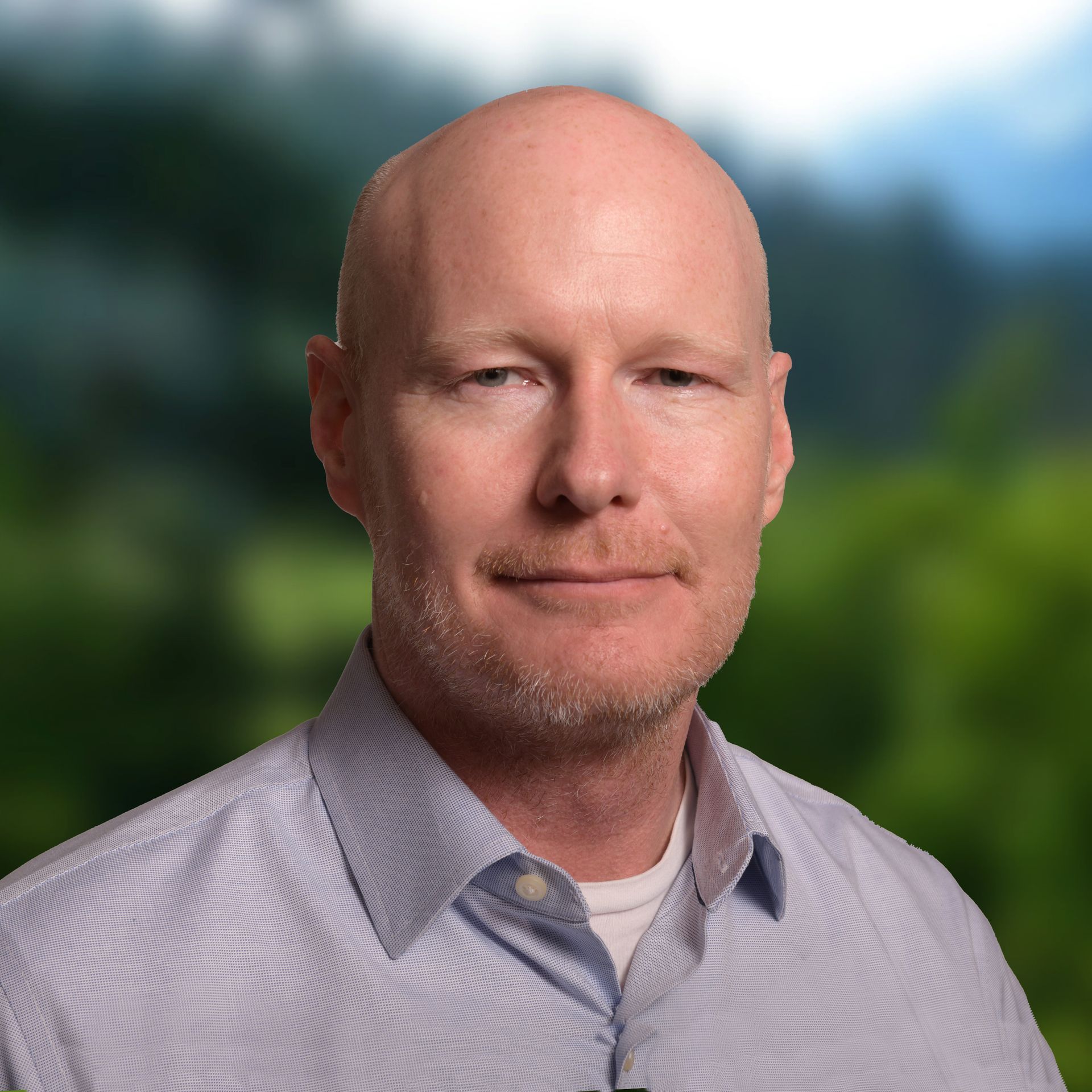 Bald man with goatee in suit smiling outdoors.