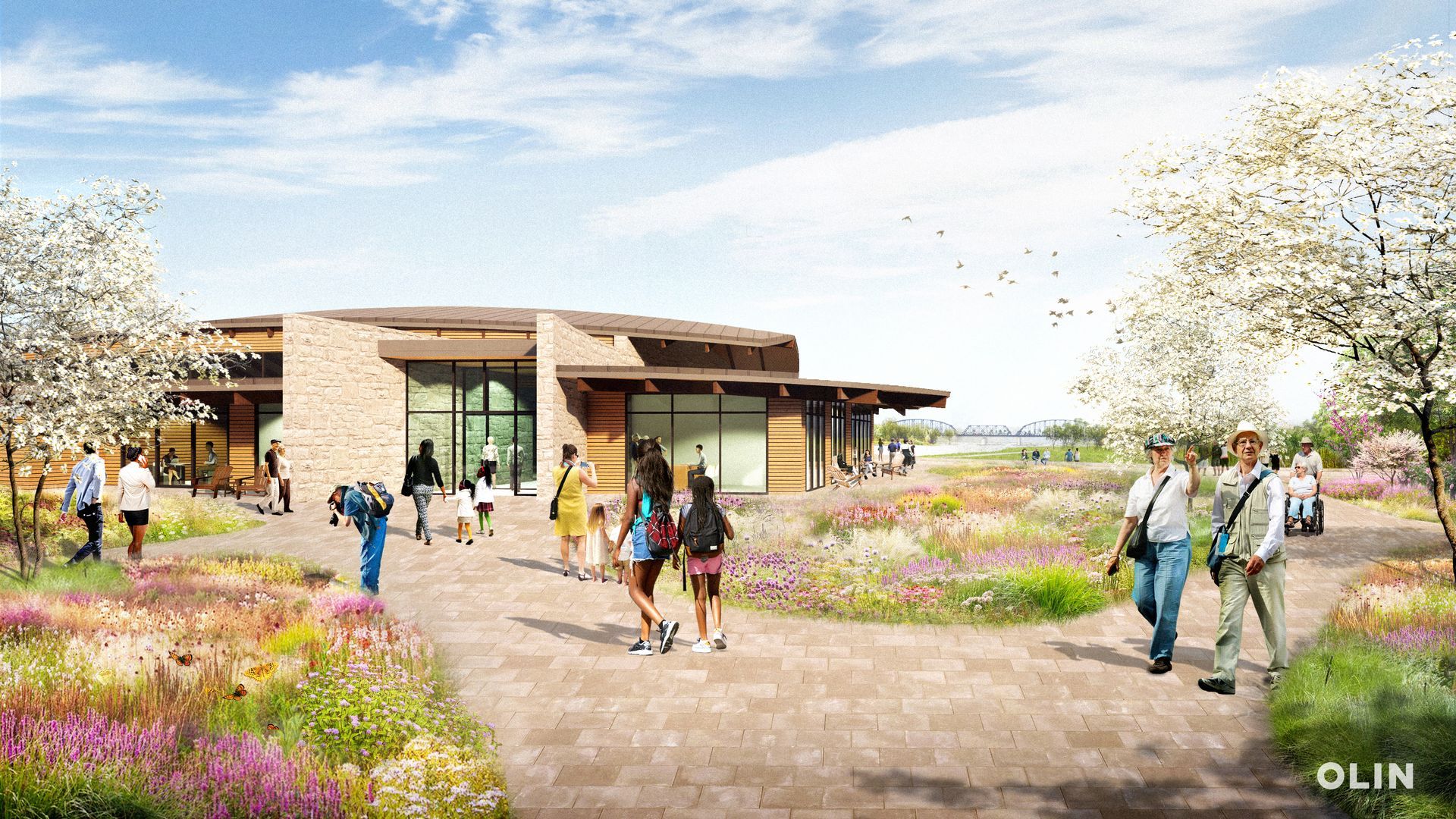 People walking on a path towards The Vista event center with a brick and wood facade, surrounded by wildflowers.