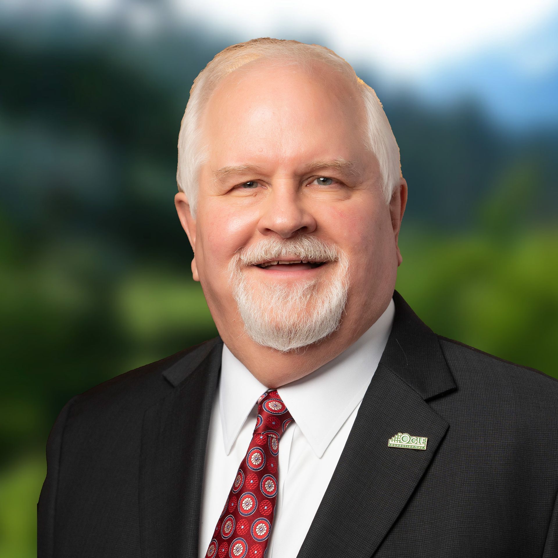 Kent Lanum in suit, smiling, against blurred green background.