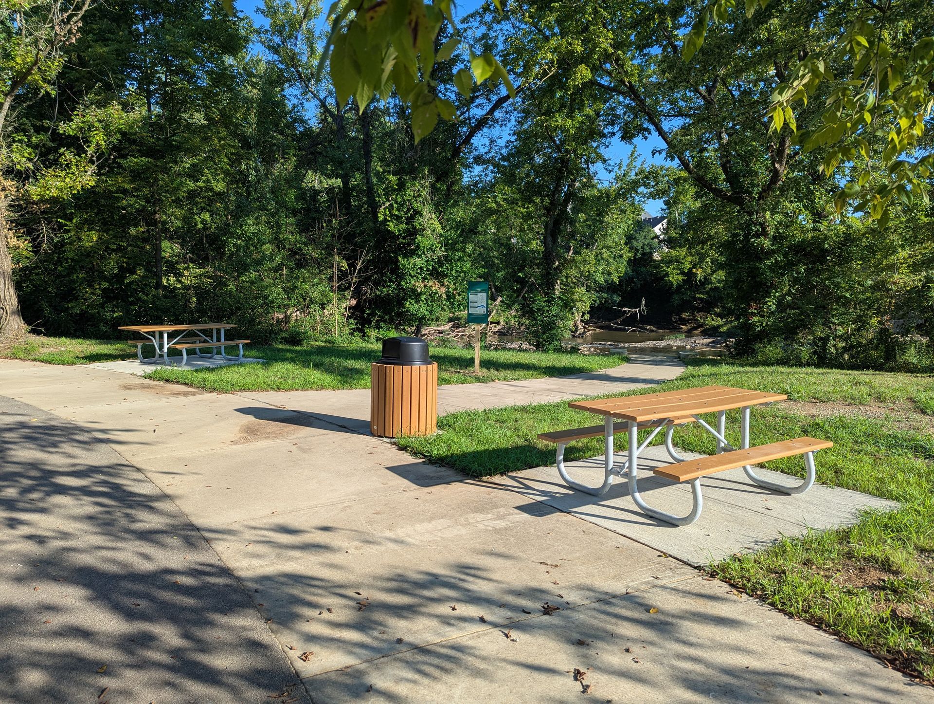 Two men setting up a picnic table on a colorful, paved area in a park with trees and trucks.