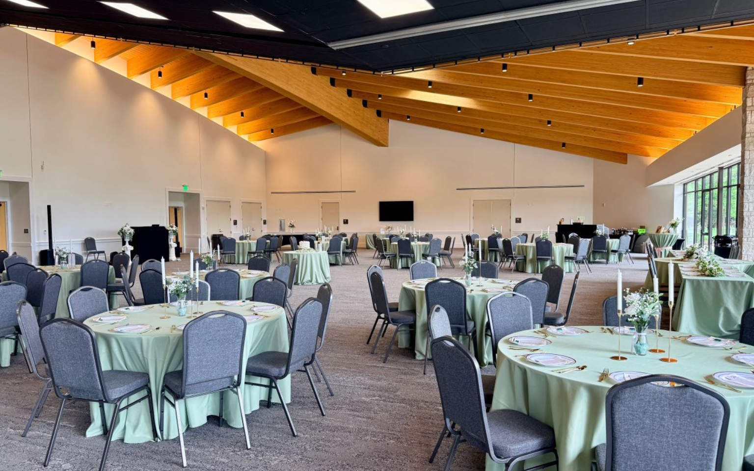 Wedding reception in a large room with round tables, white chairs, and many guests.